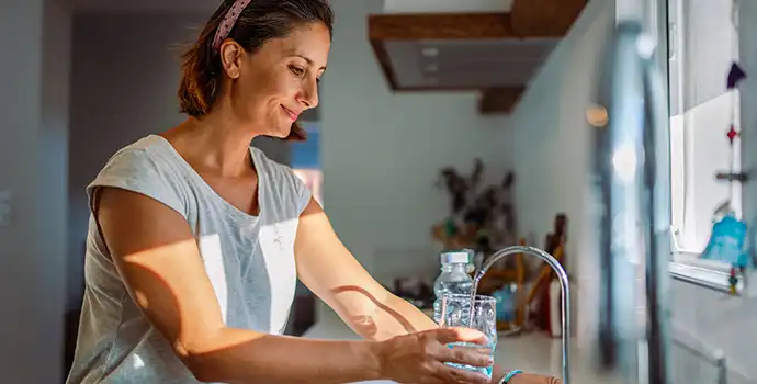 A woman drinking water from a glass in a kitchen sink.