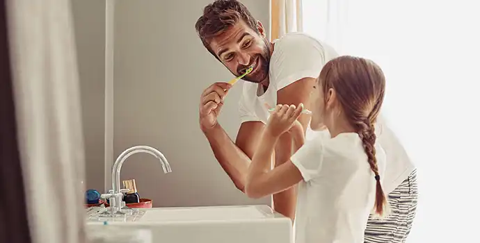 A man and a girl brushing their teeth in the bathroom.