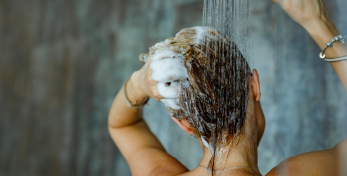 Person washing hair with shampoo under a shower.