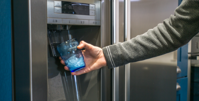A person fills a glass with water from a refrigerator's built-in dispenser.