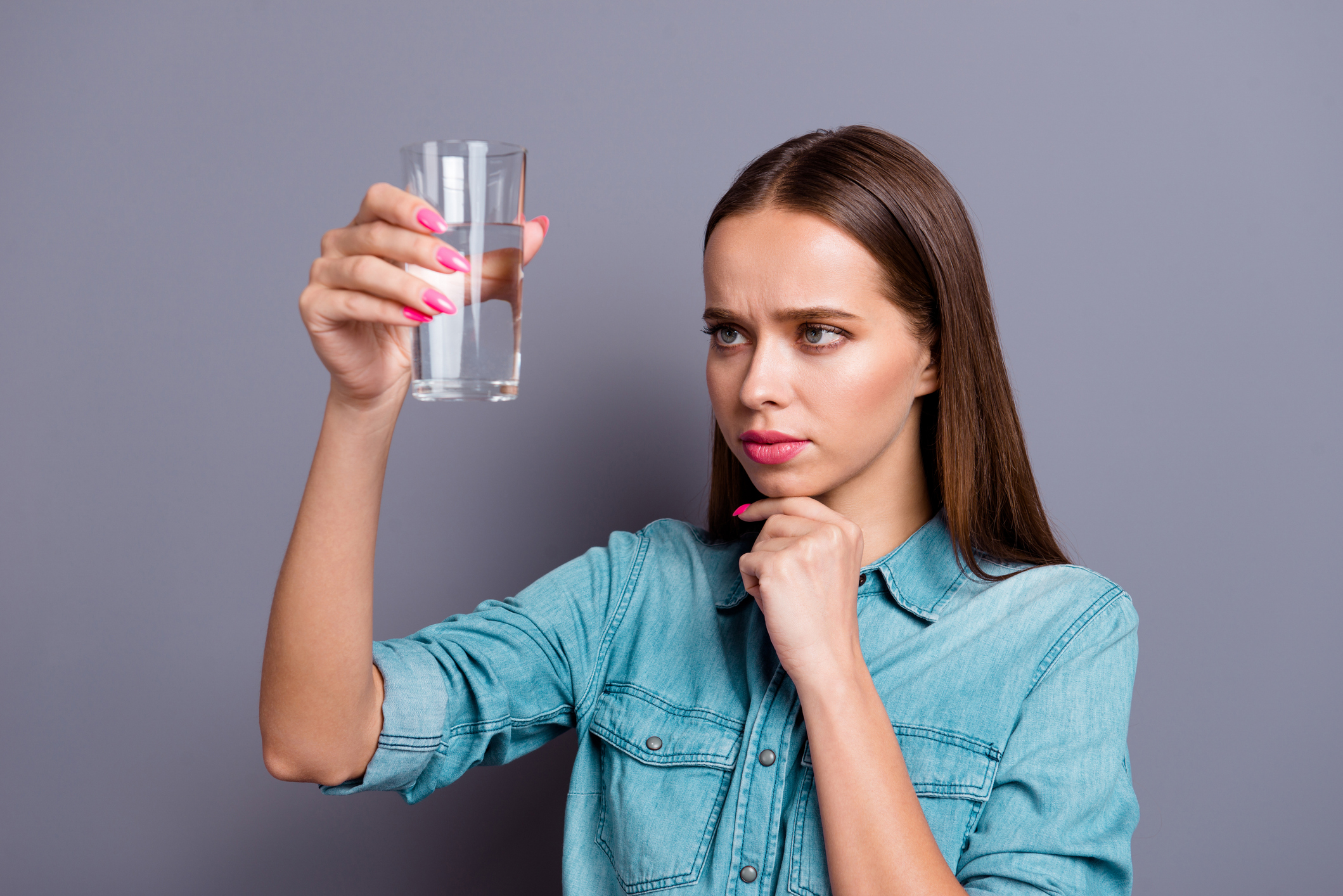 Woman examining a glass of water with a skeptical expression.