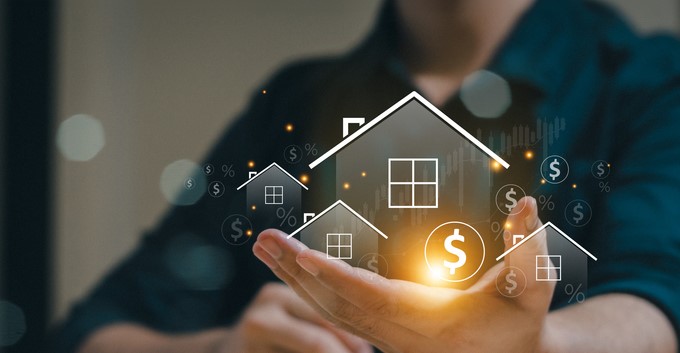 Person holding holographic house icons with dollar and percentage symbols, representing real estate investment and financial growth.