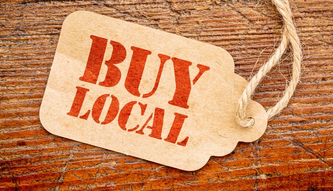 A rustic tag with the words "BUY LOCAL" in red text is attached by a string to a wooden surface.