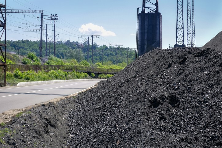 Large piles of coal beside a road with utility poles and green hills in the background.