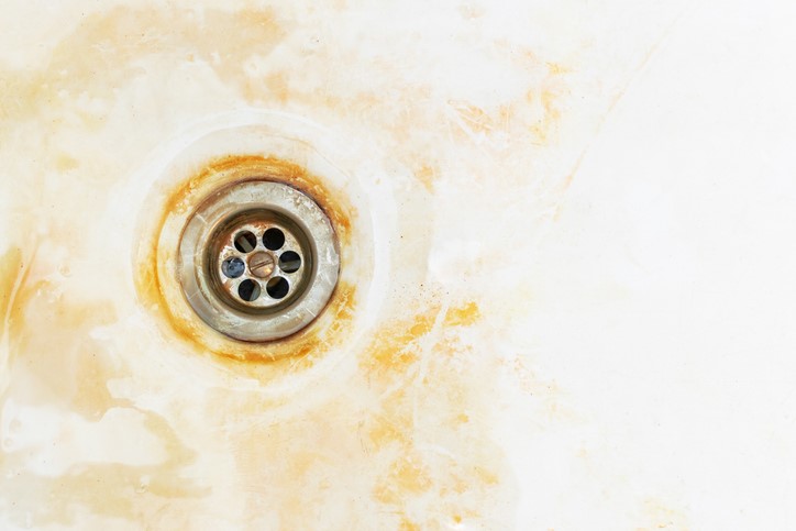 A sink drain surrounded by rust and stains.