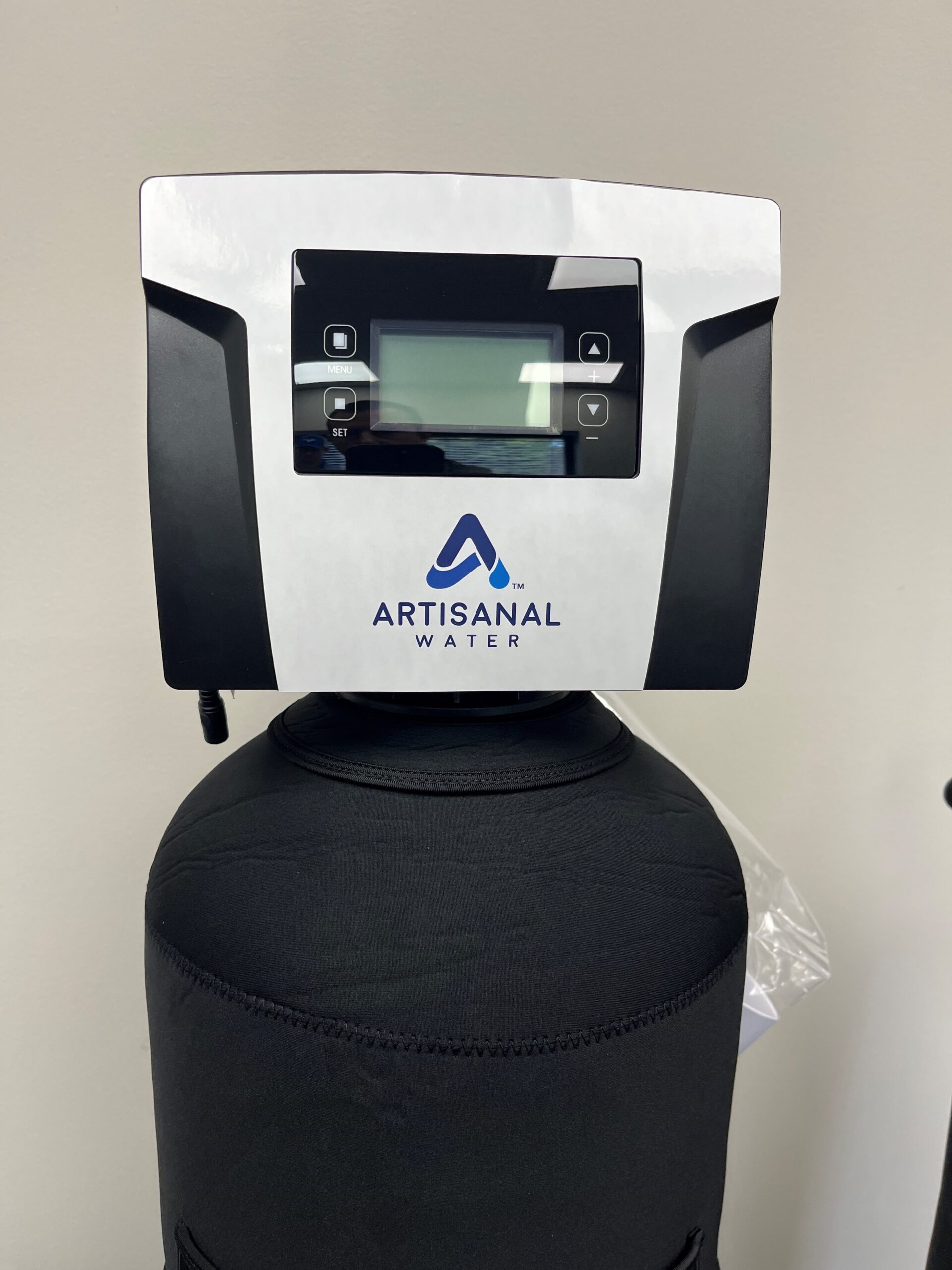 Close-up of a water filtration system control panel with a digital screen and buttons. The label reads "Artisanal Water.