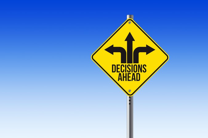 Yellow diamond-shaped sign with black arrows pointing left, right, and straight ahead, and the text "DECISIONS AHEAD" against a clear blue sky background.