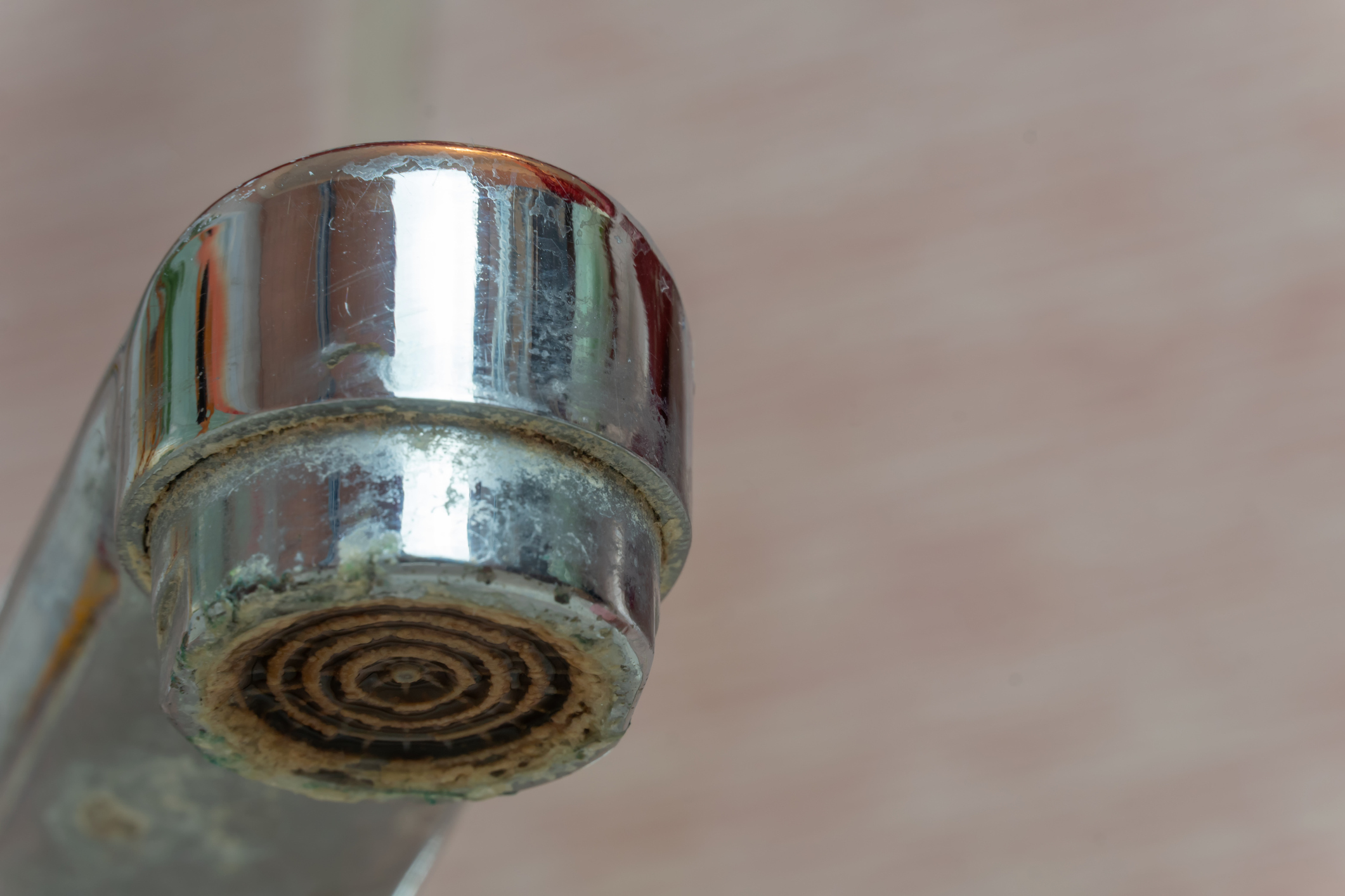Close-up of a metal faucet with visible limescale and mineral buildup around the spout against a blurred background.