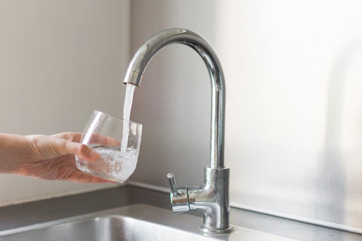 A hand holds a glass under a running kitchen faucet, filling it with water.