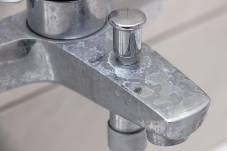 Close-up of a metal bathroom faucet with visible lime scale and hard water stains on its surface.