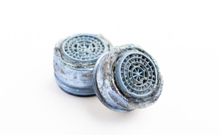 Two faucet aerators with visible mineral buildup and corrosion on a white background.