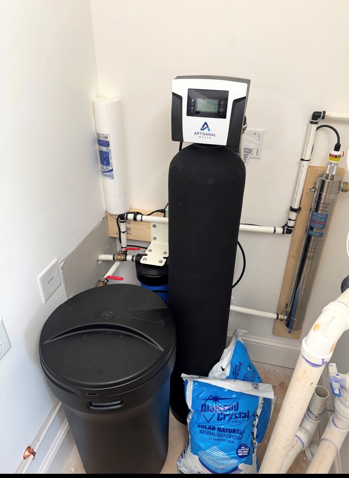 Water softening and filtration system with a brine tank, black mineral tank, and UV filter installed in a corner.